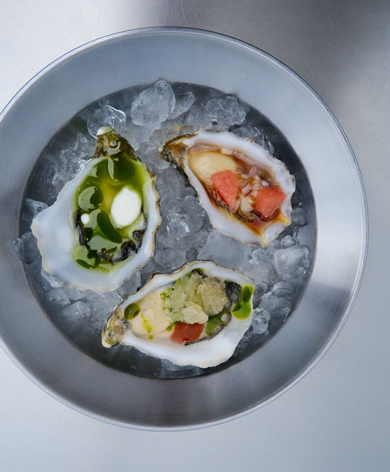Trio of dressed oysters on ice in a metal bowl